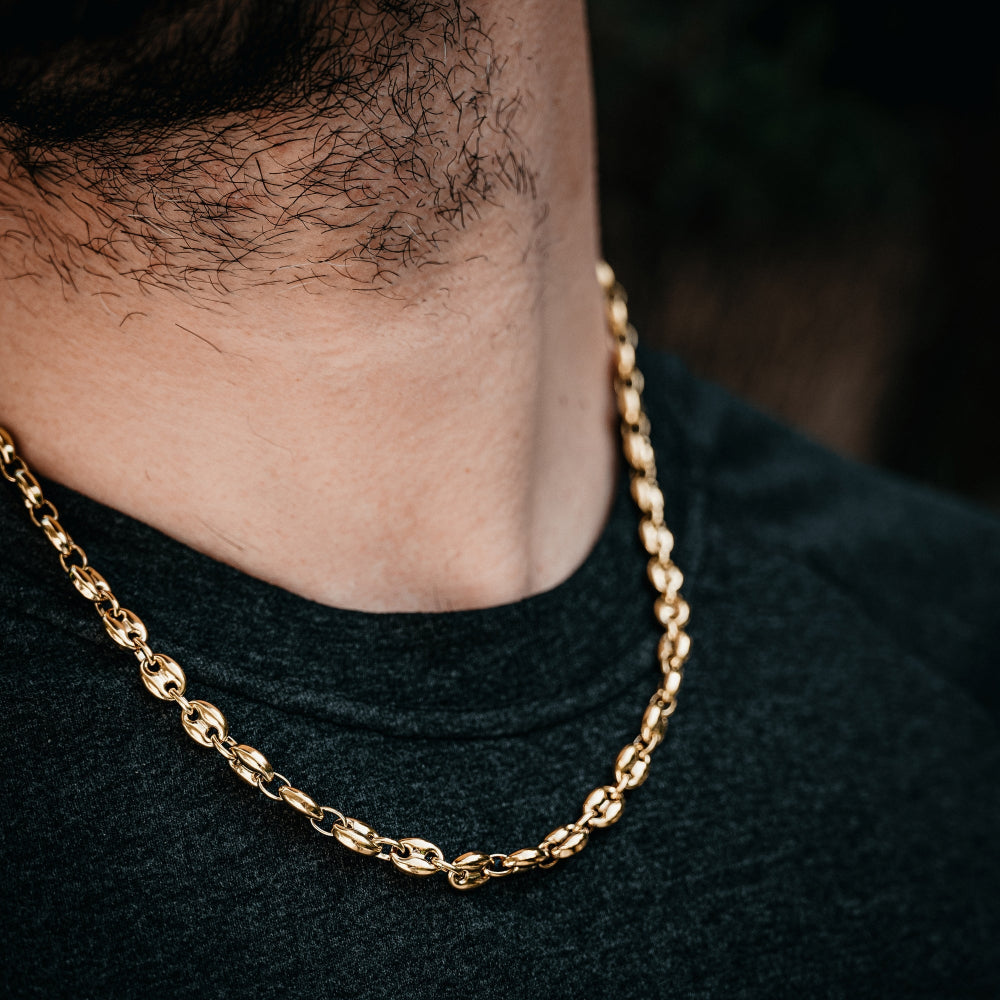 Gold chain necklace worn by a person with a dark shirt.
