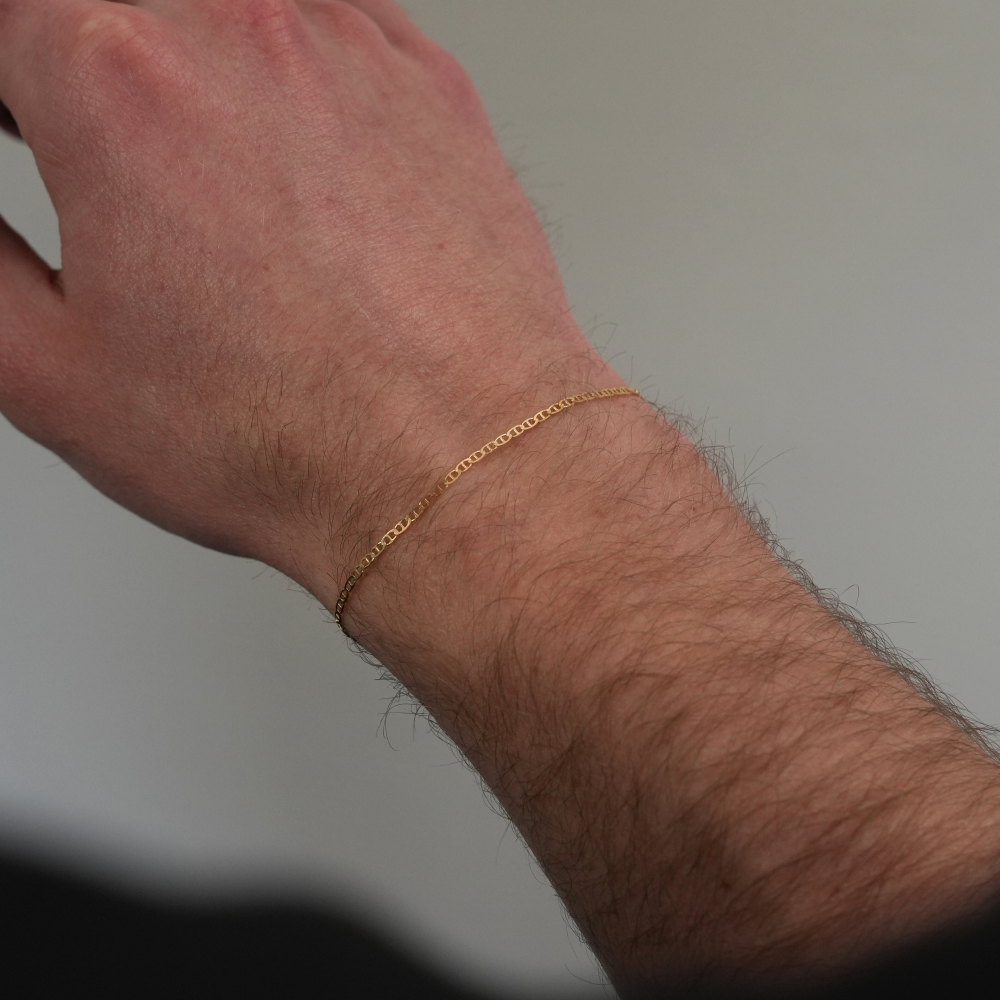 Close-up of a person's arm wearing a gold bracelet against a neutral background