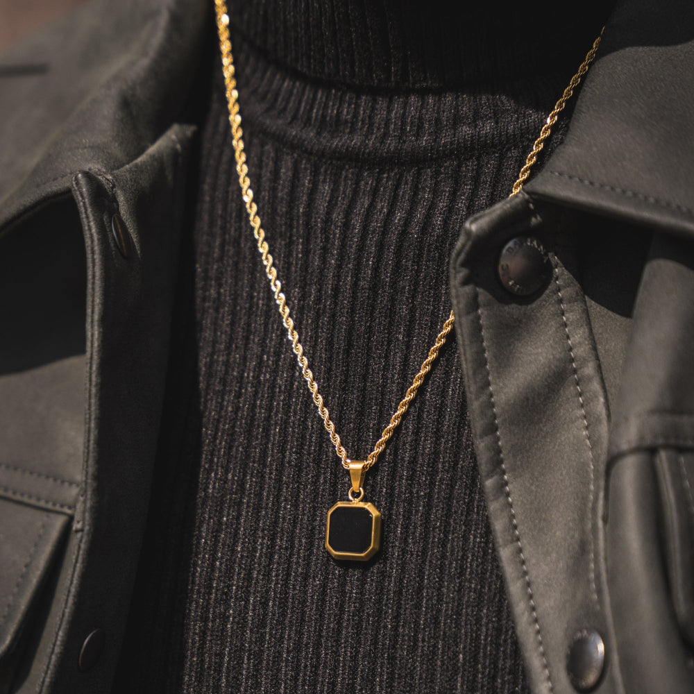 Gold necklace with a black pendant on a person wearing a black sweater and coat.