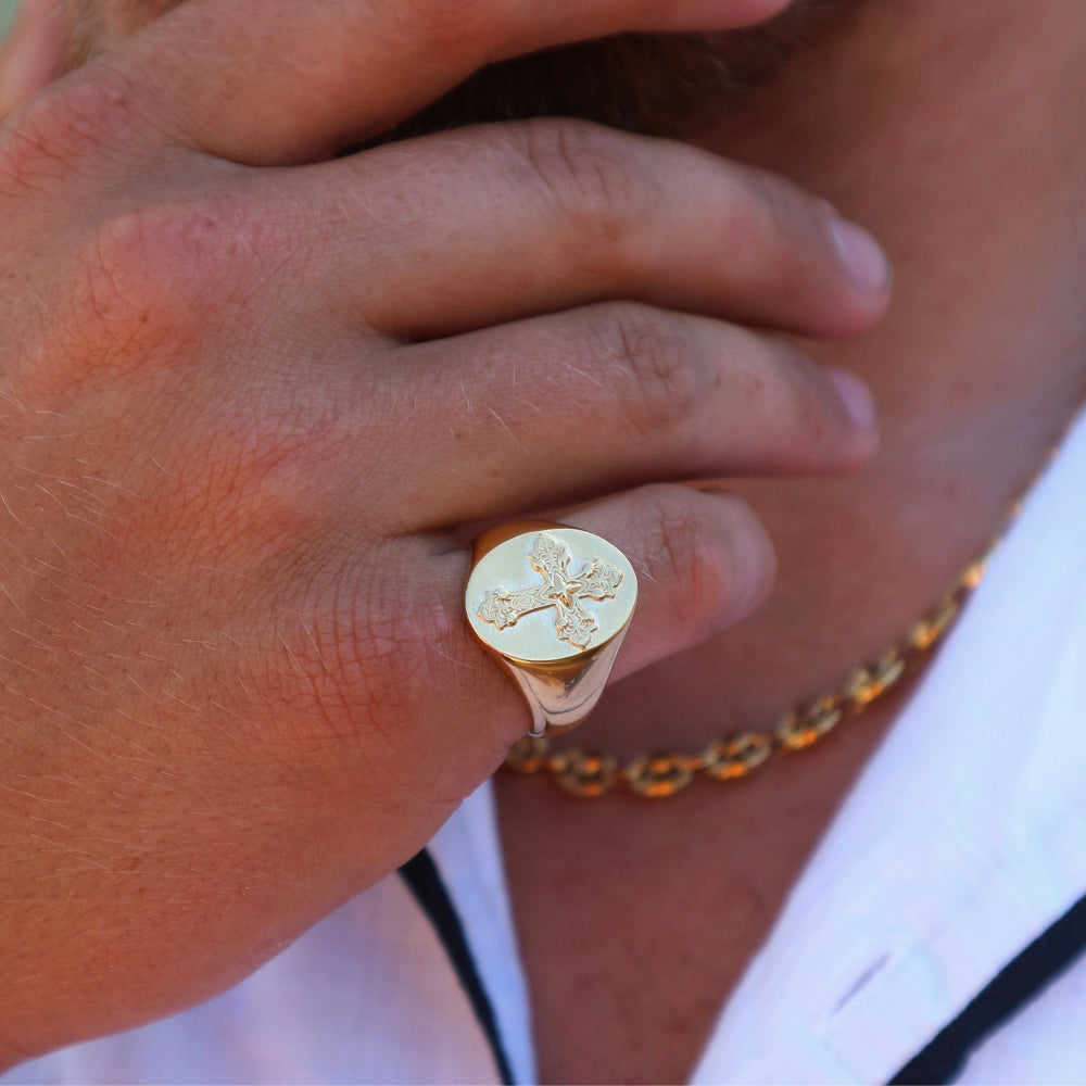 Close-up of a hand wearing a gold ring with a cross design.