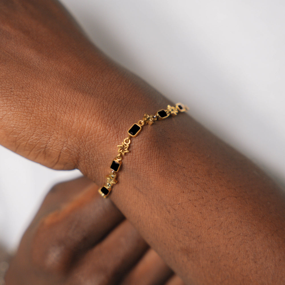 Gold bracelet with black stones on a wrist against a neutral background