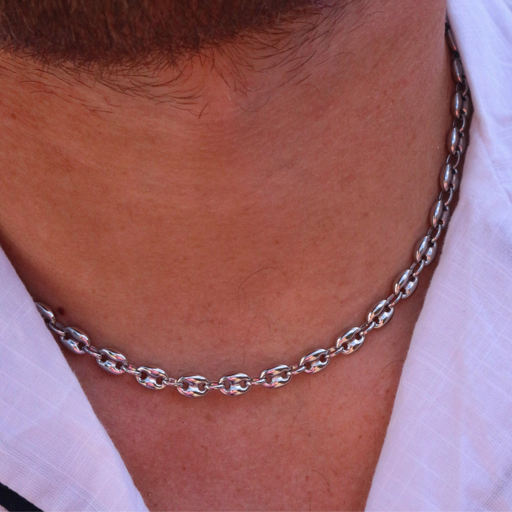 Close-up of a silver chain necklace on a person wearing a white shirt.