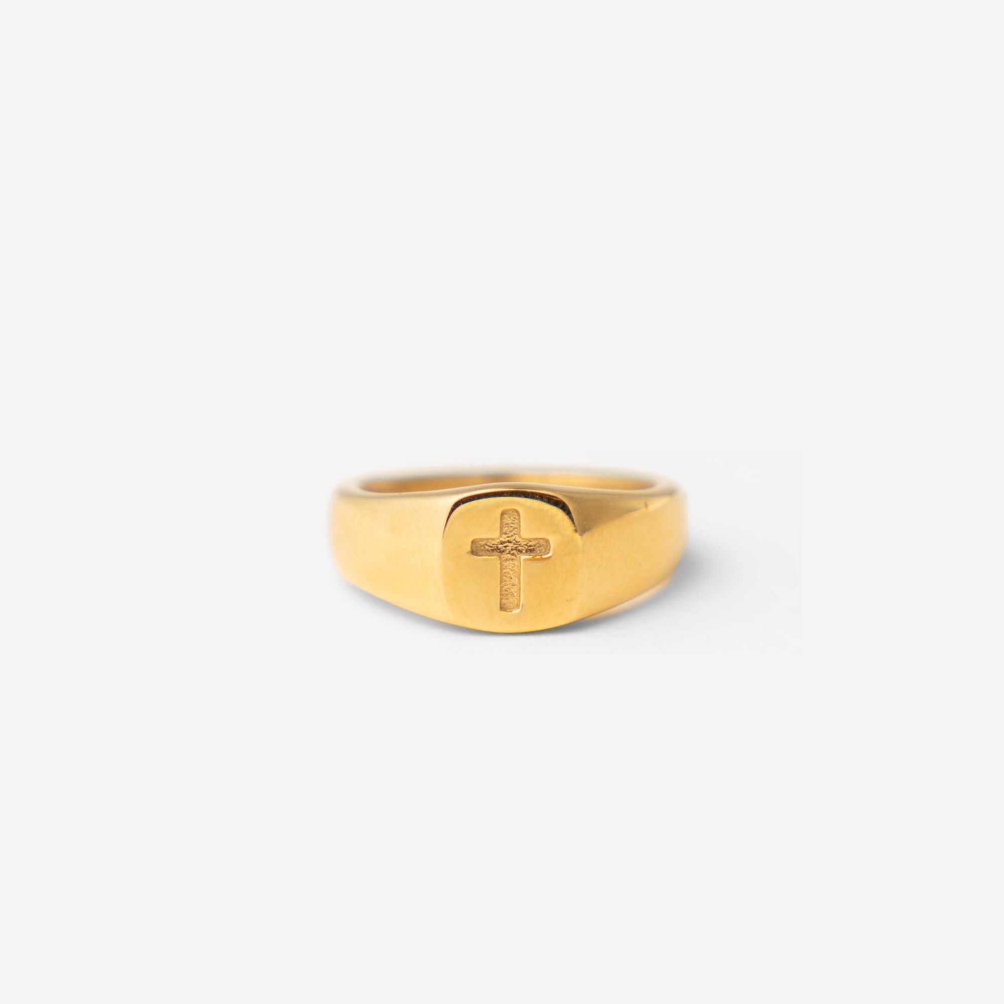 A gold signet ring with a raised cross on the face, photographed against a clean, light off-white background.