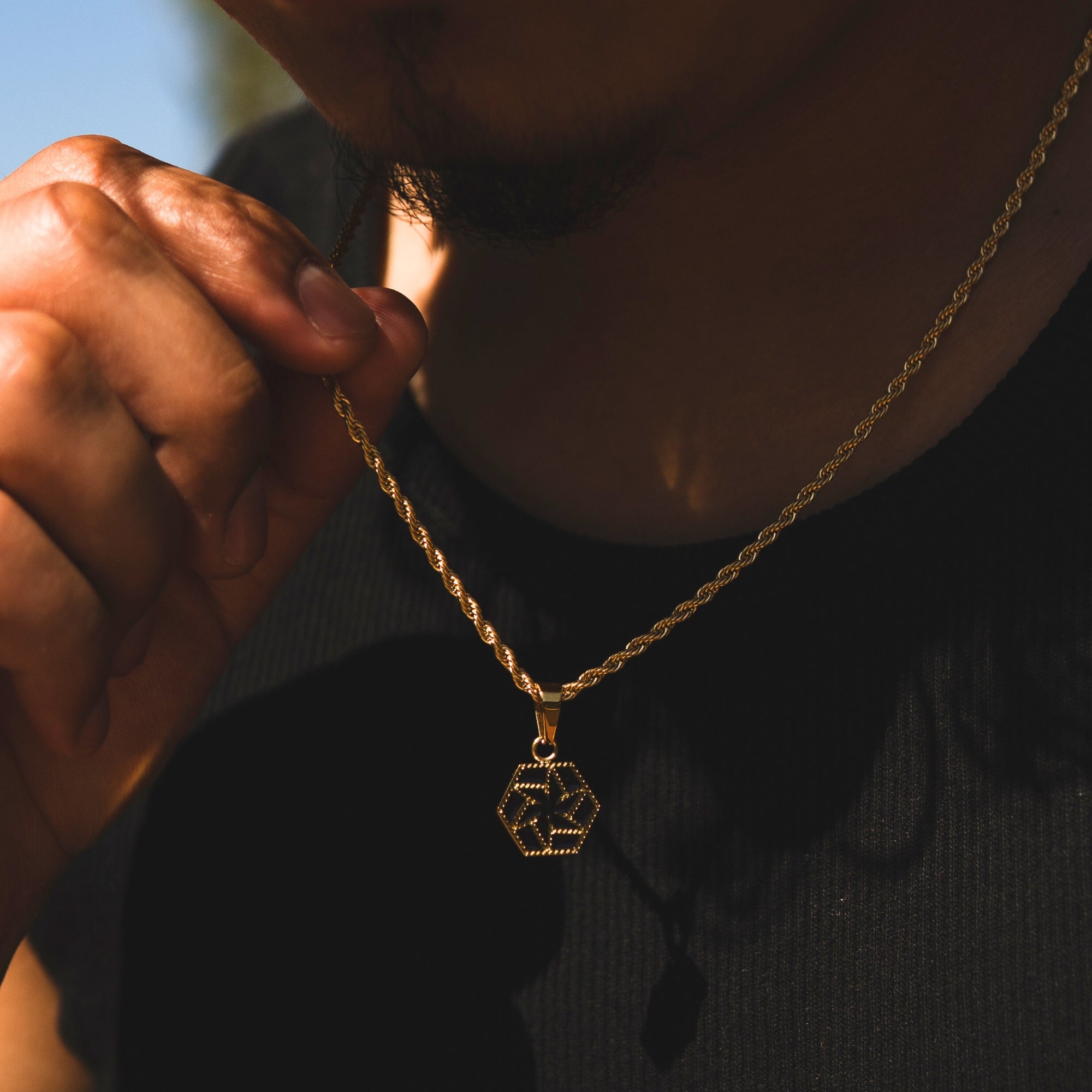 Gold necklace with a hexagonal pendant held by a person