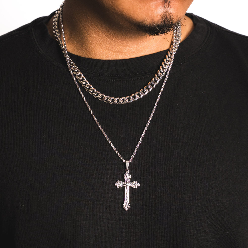 Person wearing a black shirt with two silver chain necklaces and a cross pendant.