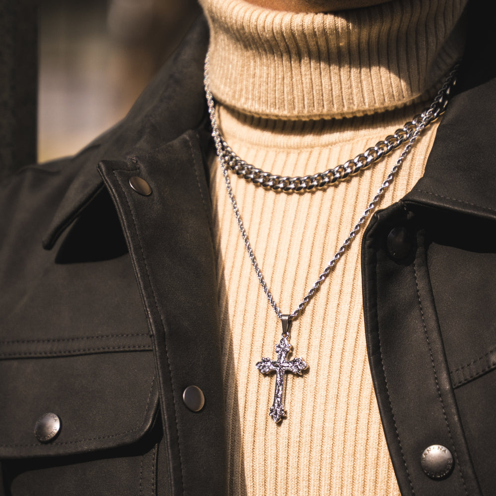 Person wearing a black jacket and beige turtleneck with layered necklaces, including a cross pendant.