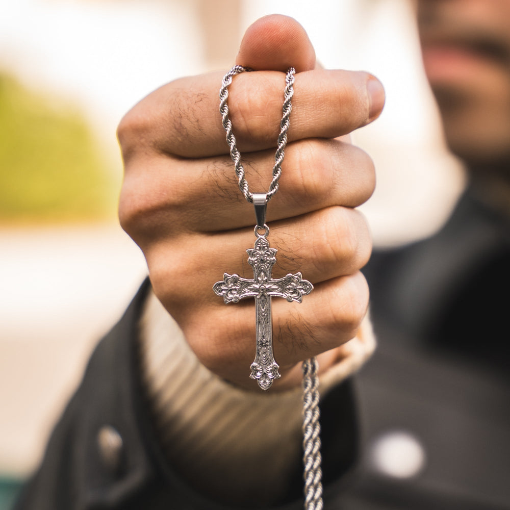 Hand holding a silver cross necklace with a blurred background