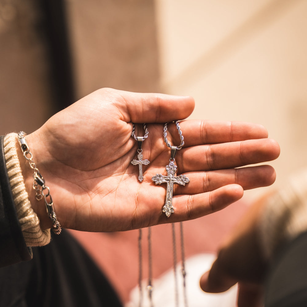 Hand holding two silver cross necklaces with a blurred background