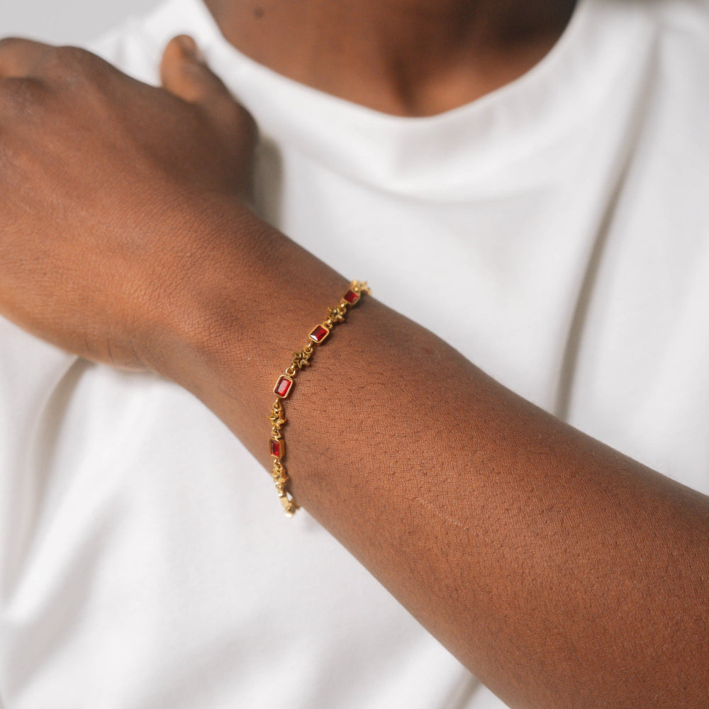 Gold bracelet with red stones on a person's wrist against a white background