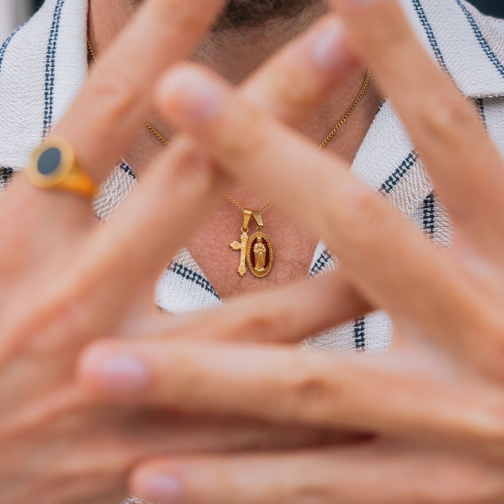 Close-up of a person wearing a gold necklace with a pendant, with hands covering the face.