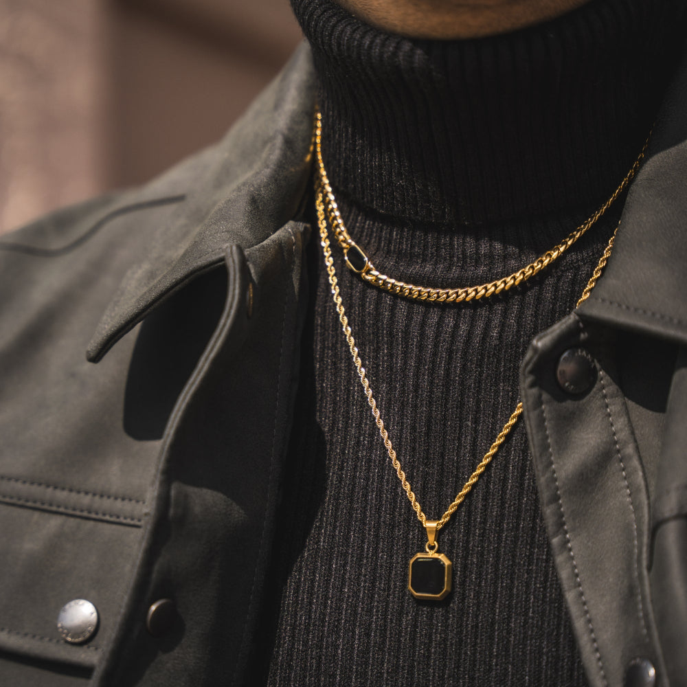 Person wearing a black turtleneck and gold chain necklace with a square pendant.