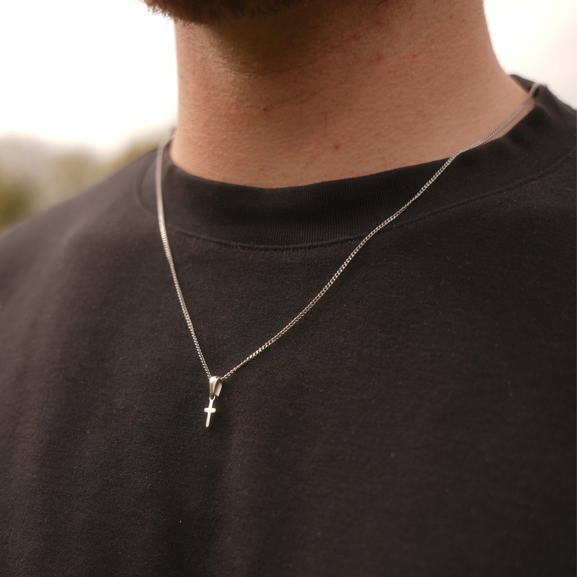 Person wearing a black shirt with a silver necklace featuring a cross pendant.