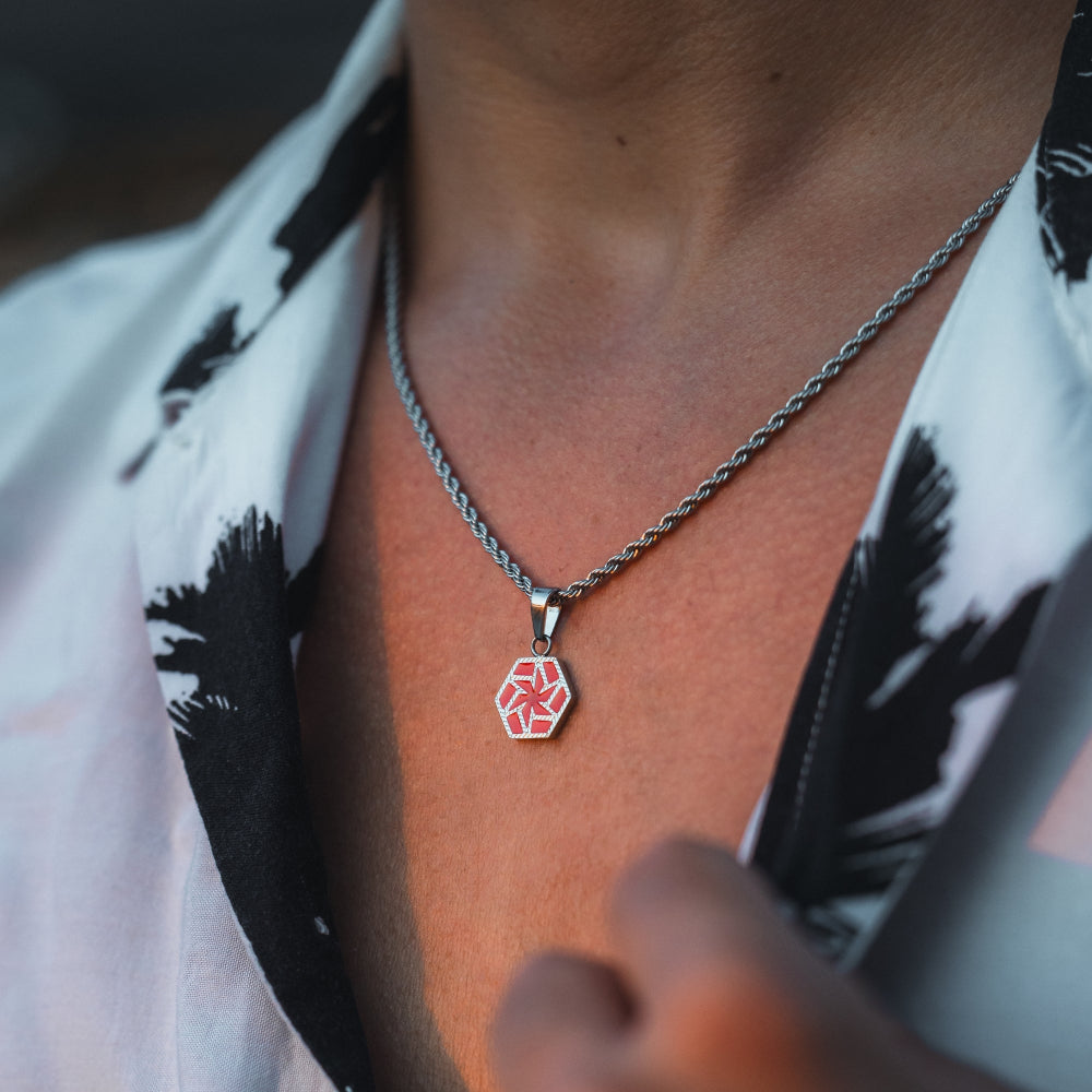 Person wearing a necklace with a red hexagonal pendant, blurred background