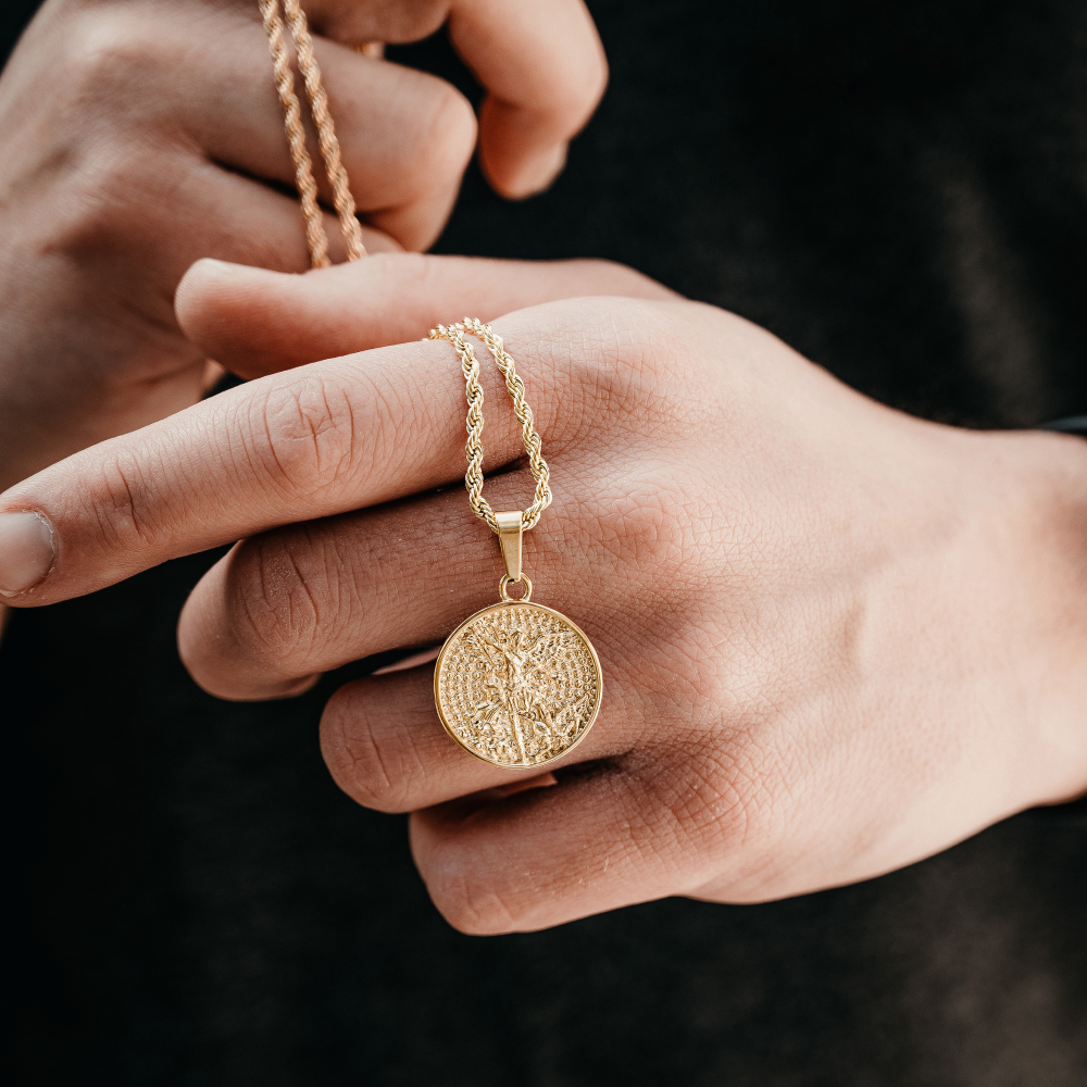 Gold necklace with a round pendant held by hands against a dark background