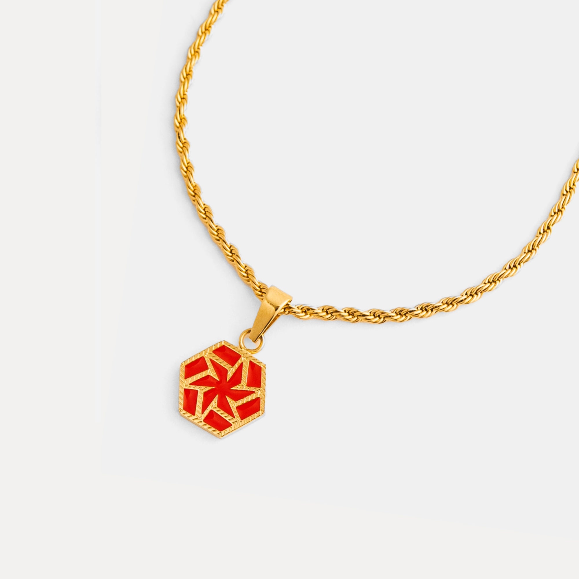 Gold necklace with a red hexagonal pendant on a white background