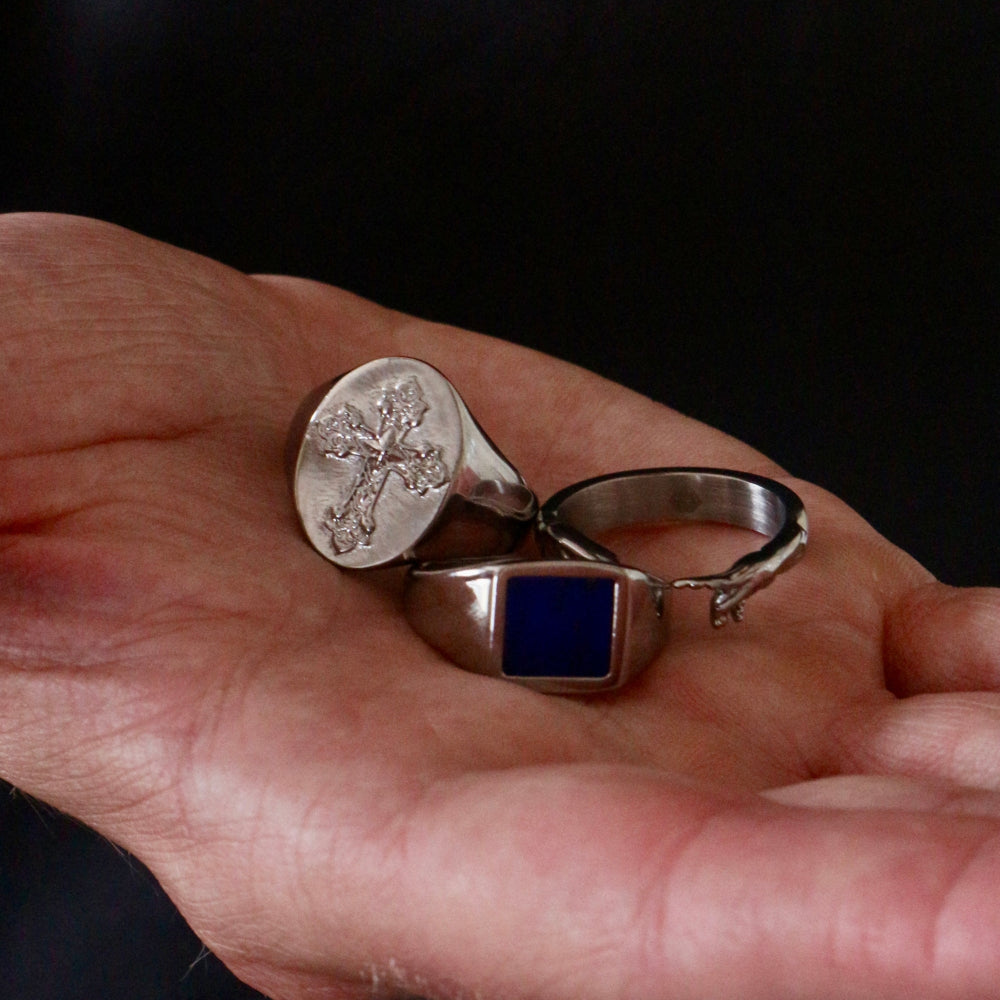 Two silver rings with engraved designs on a person's hand against a dark background