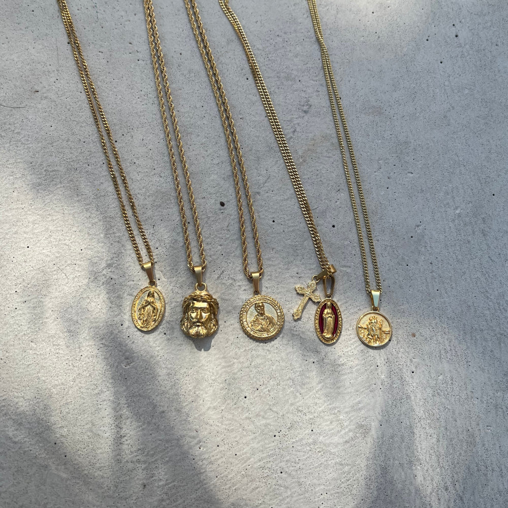 Five gold necklaces with various pendants on a textured gray surface
