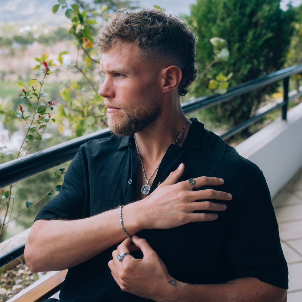 Man in a black shirt standing outdoors with greenery in the background