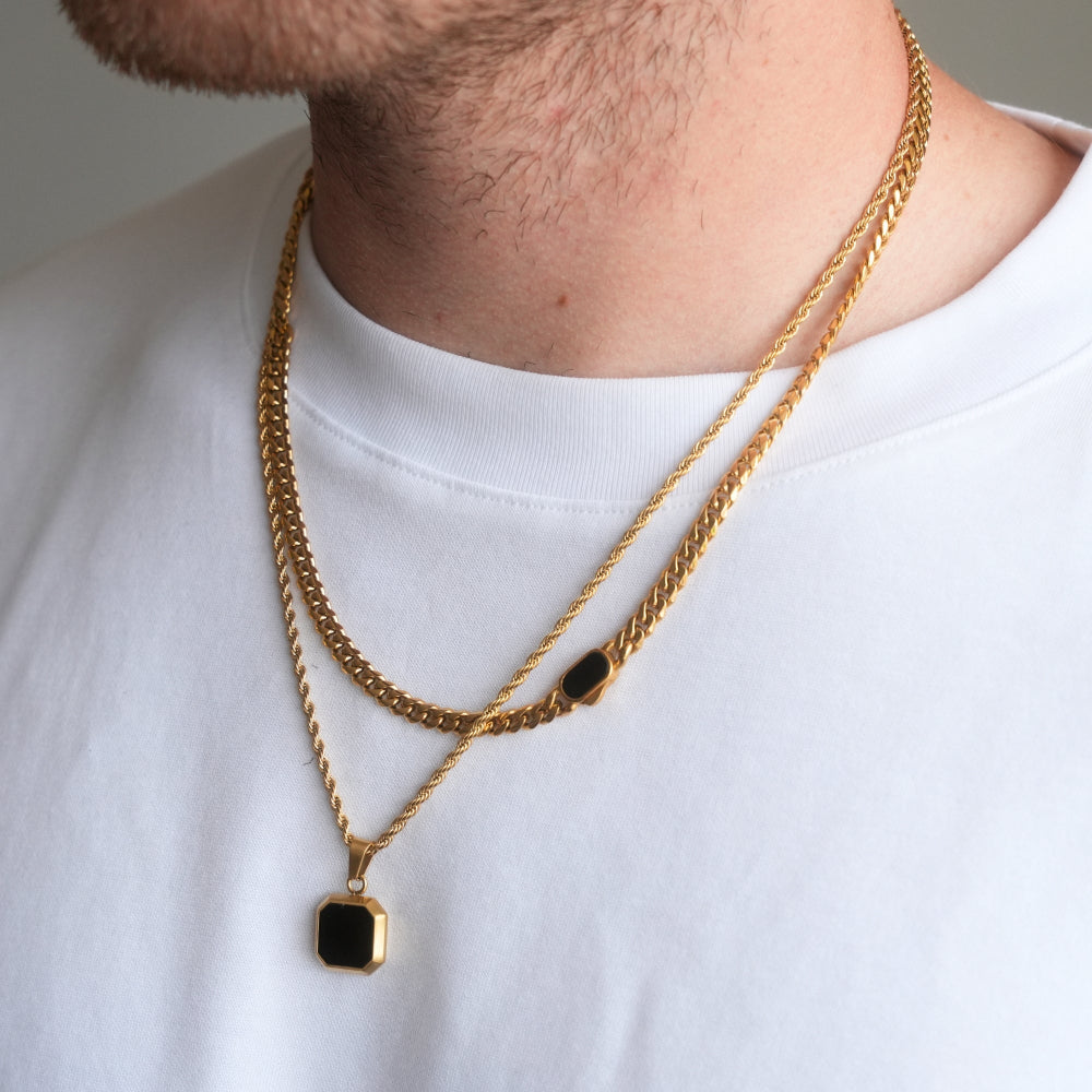 Gold chain necklace with black pendants worn by a person on a white shirt background