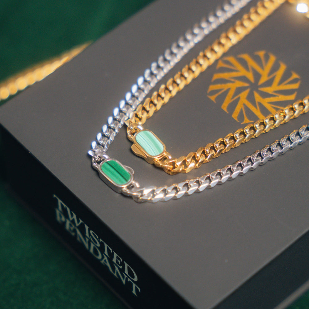 Two gold and silver chains with green pendants on a branded box.