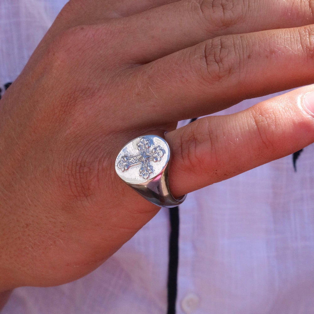 Silver ring with a cross design on a person's finger against a blurred background