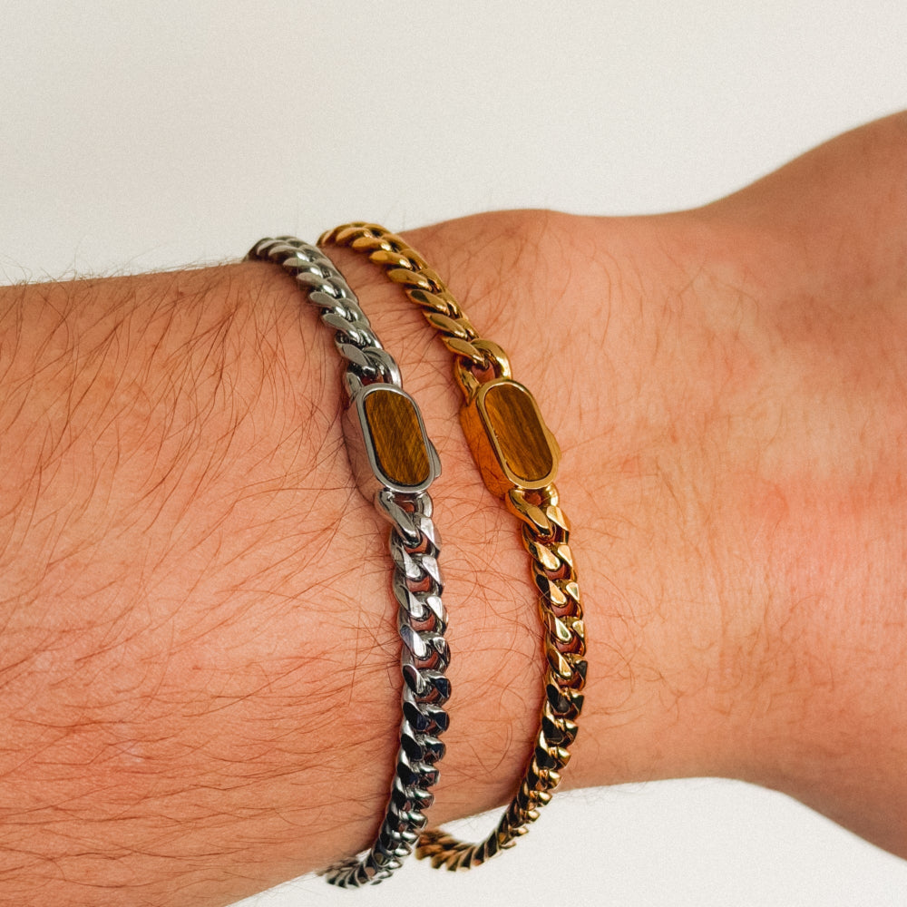 Two chain bracelets, one gold and one silver, on a wrist against a neutral background.