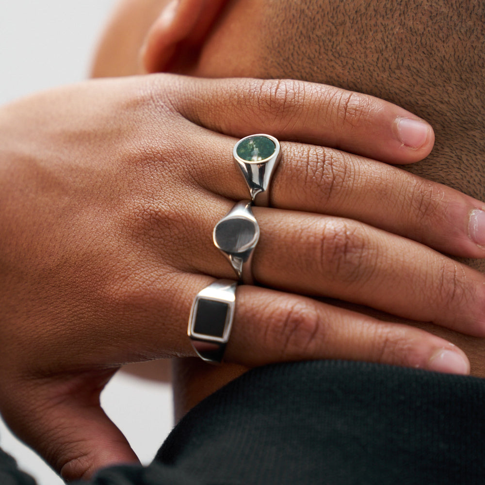 Close-up of a hand wearing two silver rings with gemstones on a neutral background