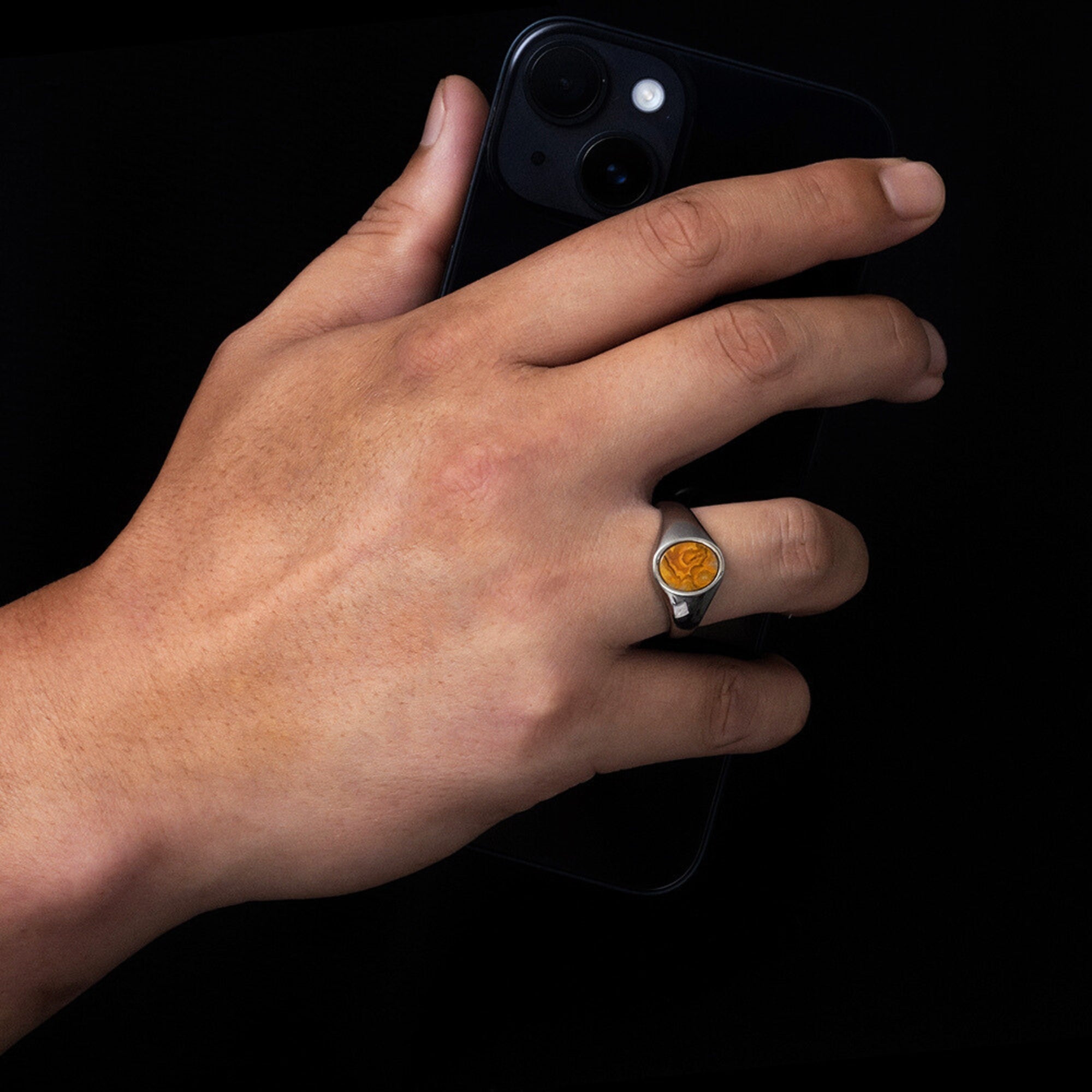 Hand wearing a ring with a stone, holding a phone on a black background