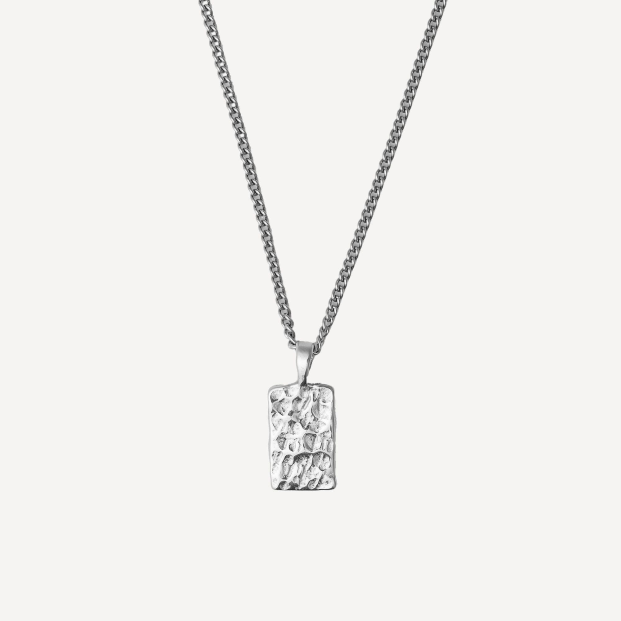 A silver rectangular pendant necklace with a textured, hammered surface, suspended from a matching silver chain against a light gray background.
