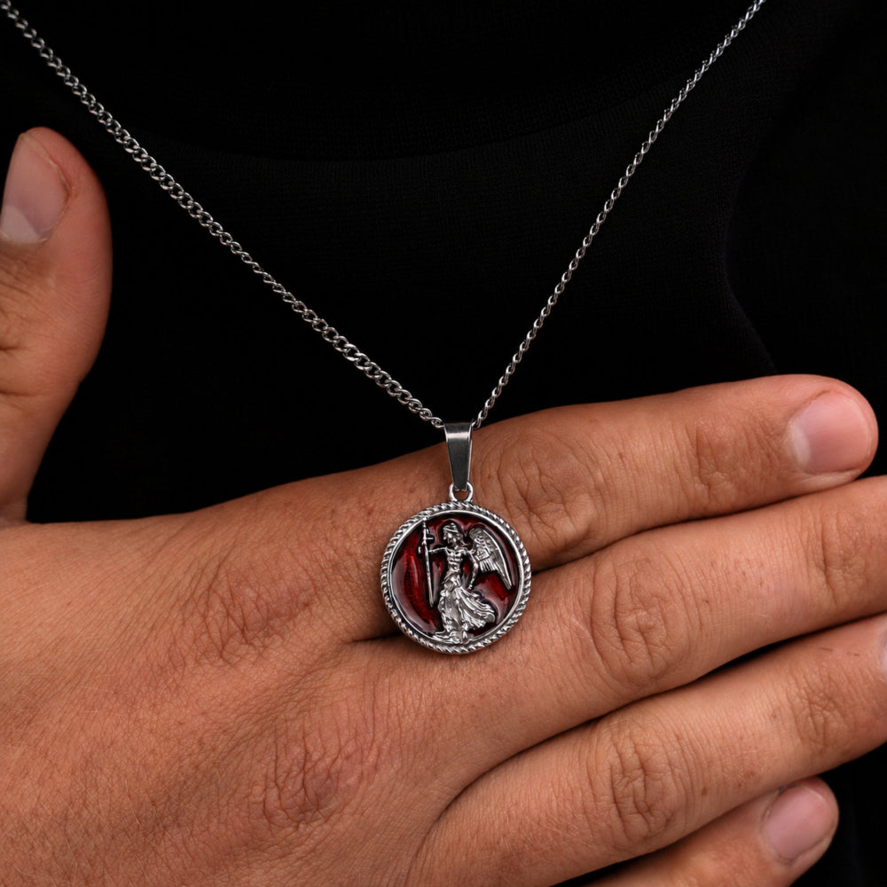 Silver necklace with a pendant held by a hand against a black background