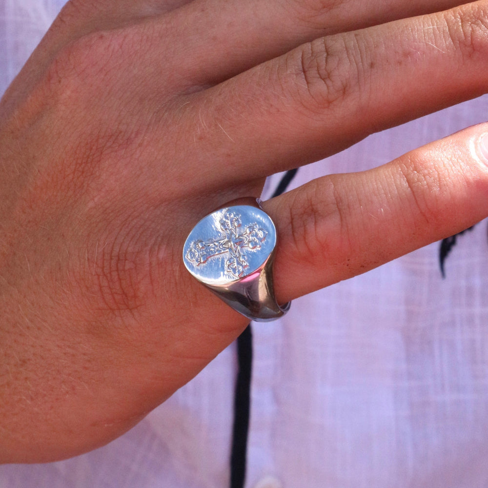 Silver ring with a floral design on a person's finger against a white background
