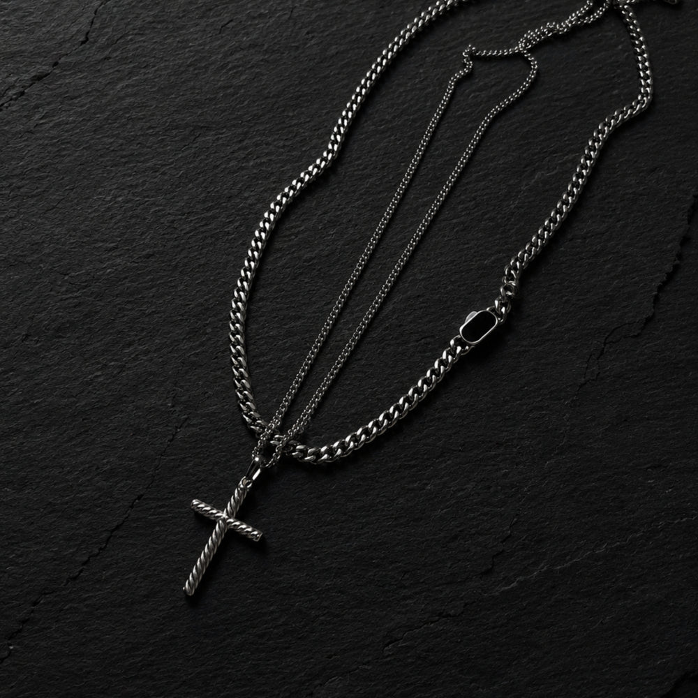 Silver chain necklace with a cross pendant on a black textured background