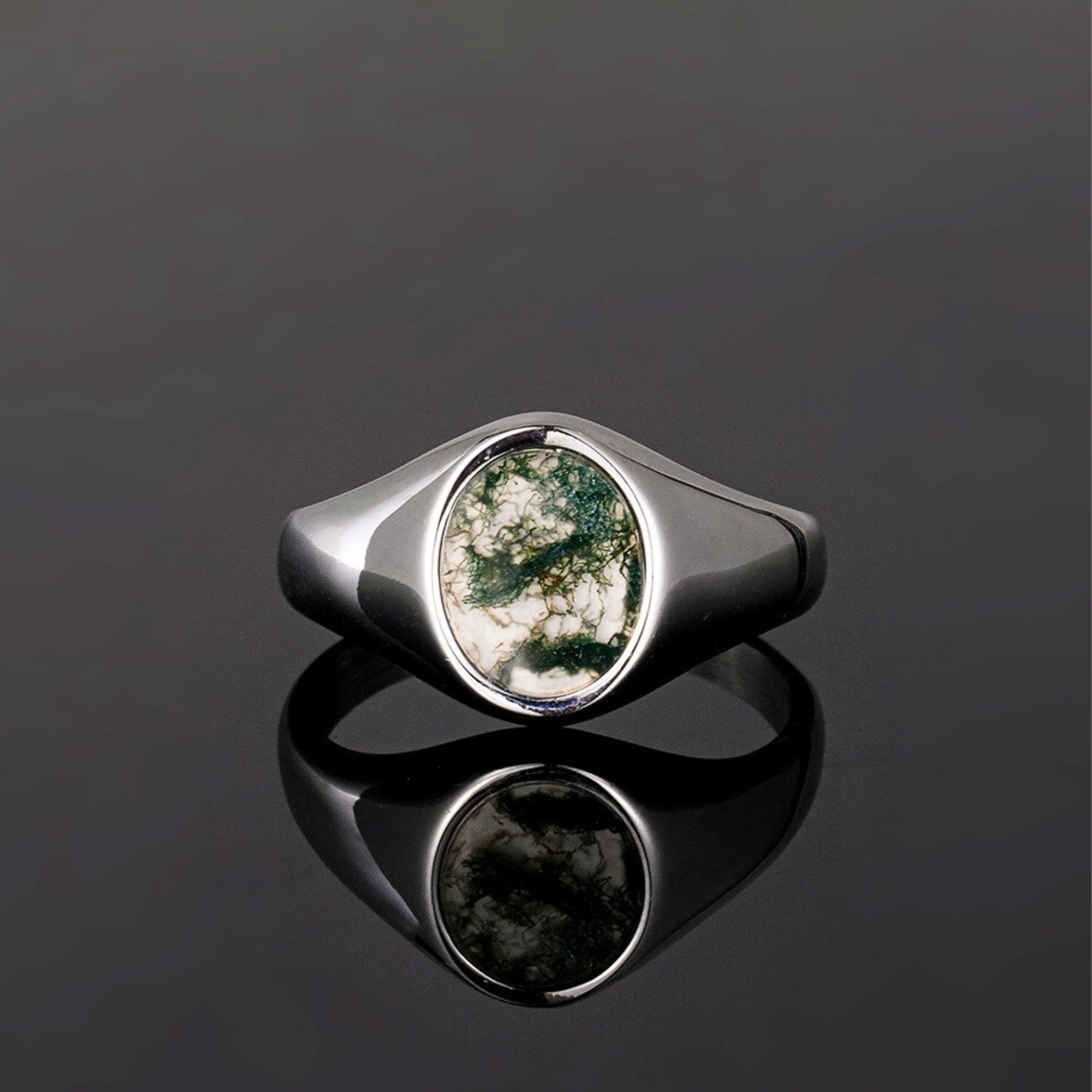 Silver ring with a green stone on a reflective black surface