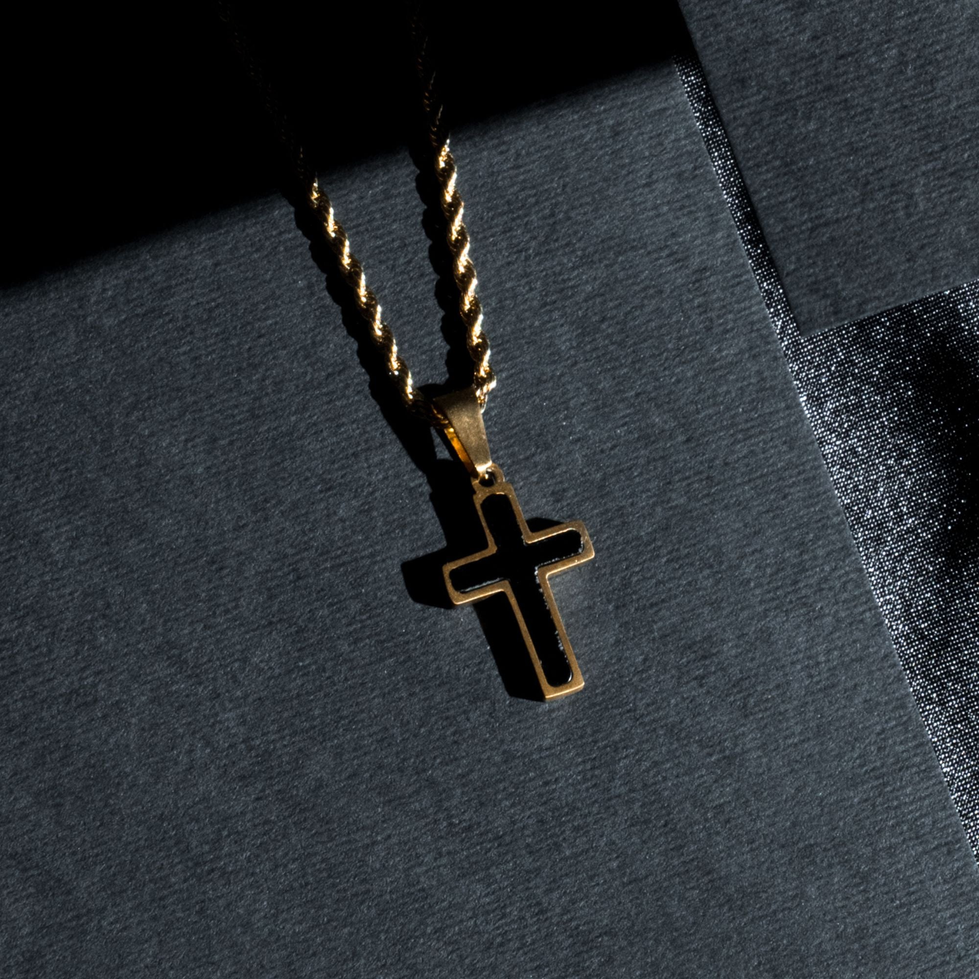A gold cross pendant necklace with a twisted rope chain, displayed on a dark textured surface with dramatic shadow lighting.