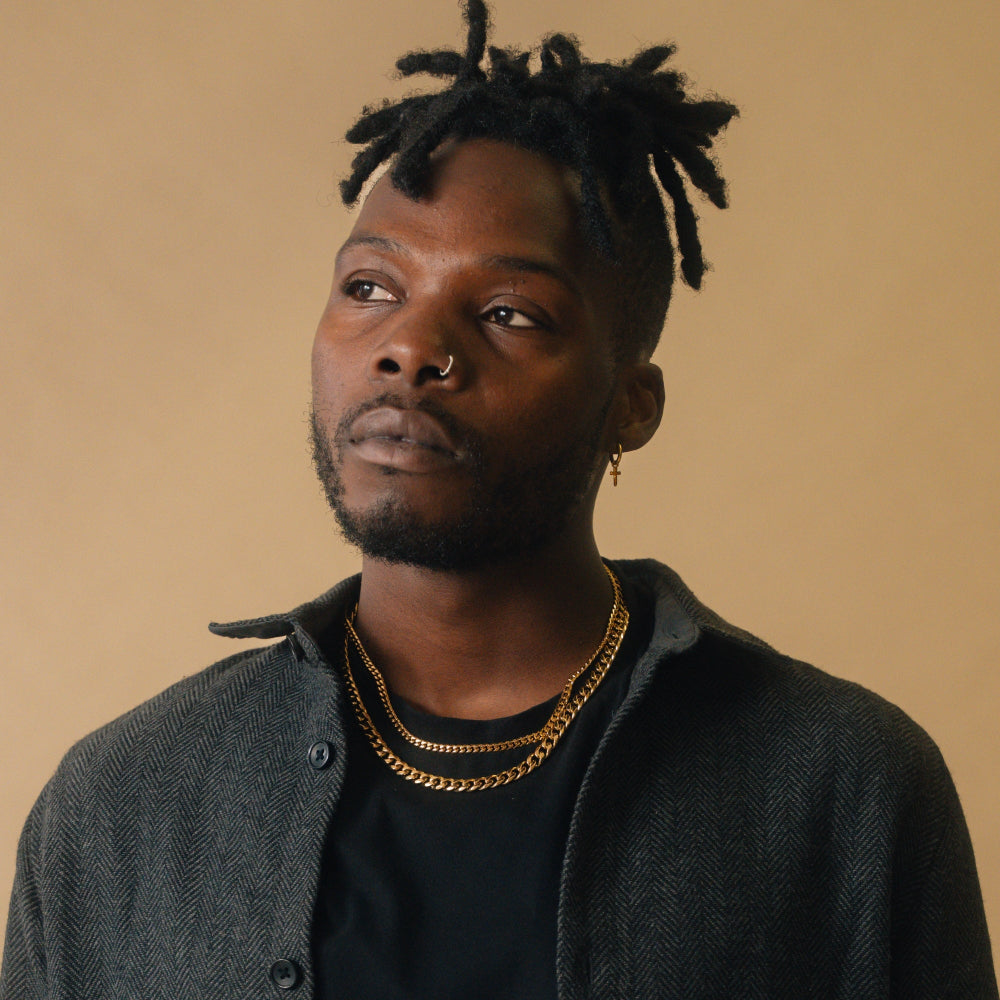 Man wearing a dark jacket and gold chain necklace against a beige background