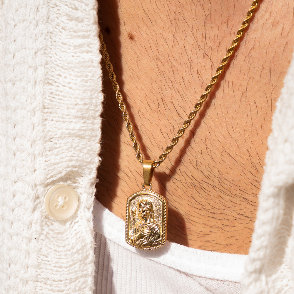 Gold necklace with a pendant on a person wearing a white textured garment.
