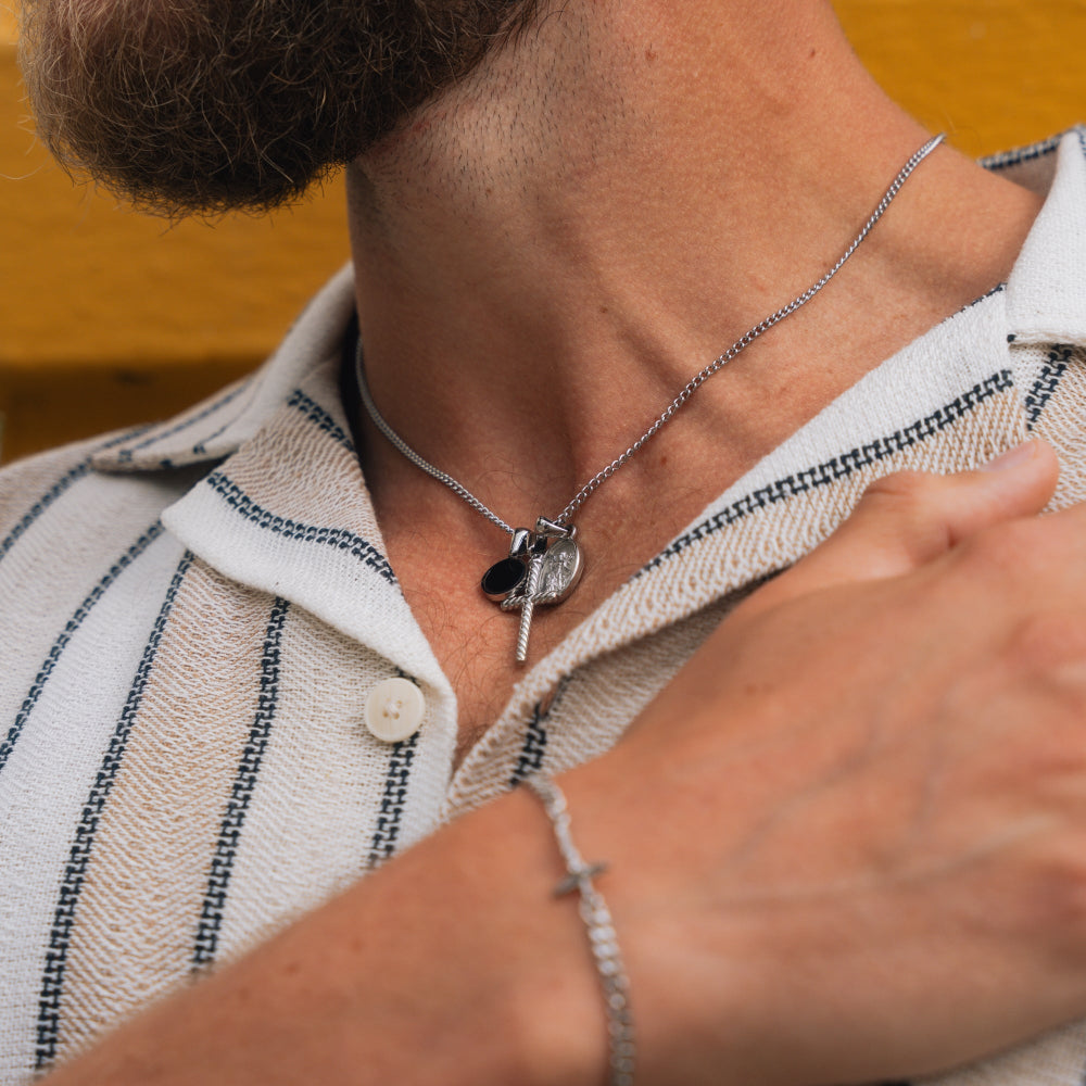 Person wearing a necklace with a key pendant and a bracelet on a neutral background