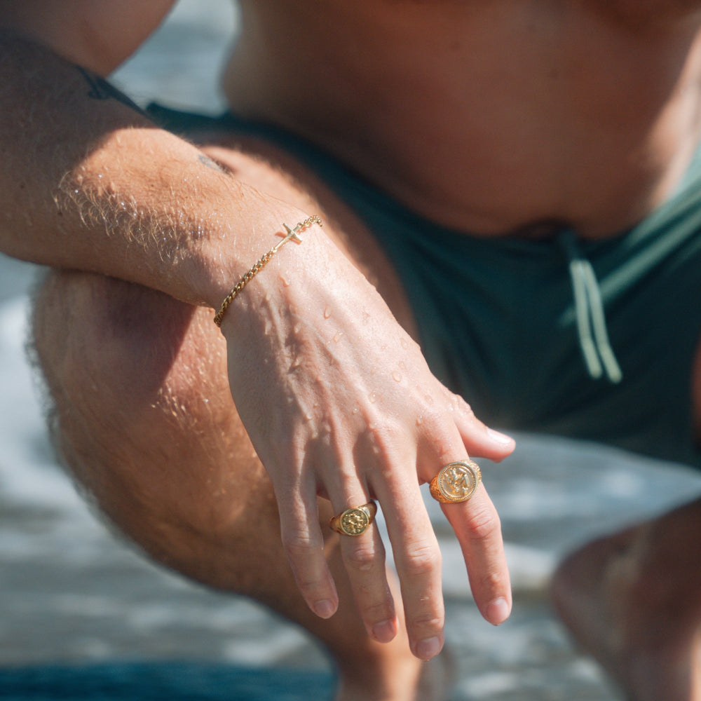 Close-up of a person's hand with gold rings and bracelet by a body of water.
