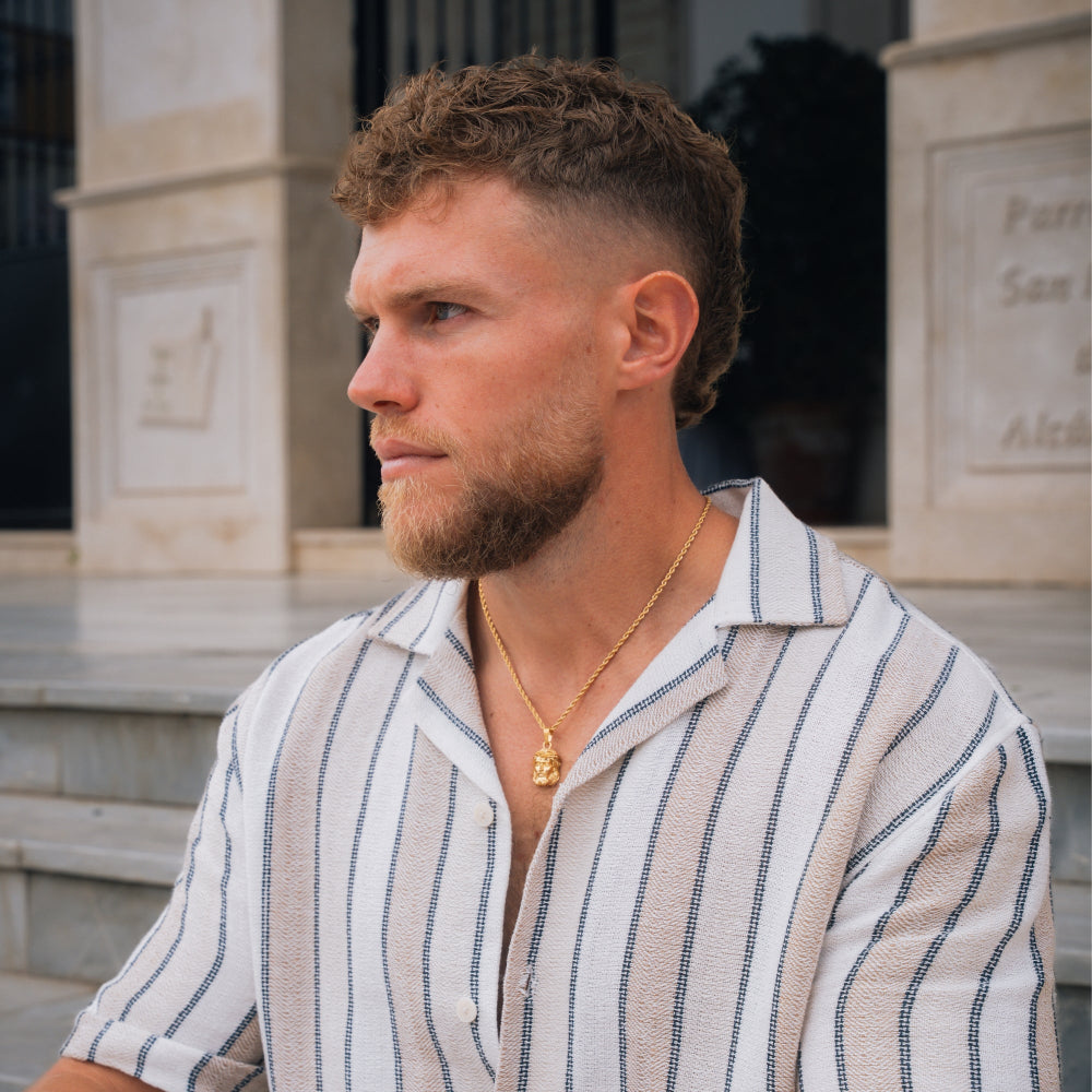 Man wearing a striped shirt and gold necklace in front of a building
