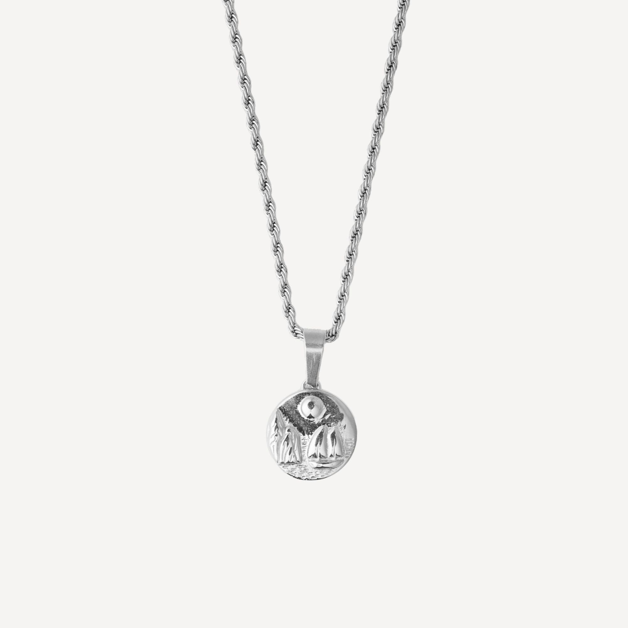A silver chain necklace with a small round pendant featuring a detailed relief design, shown against a plain light gray background.