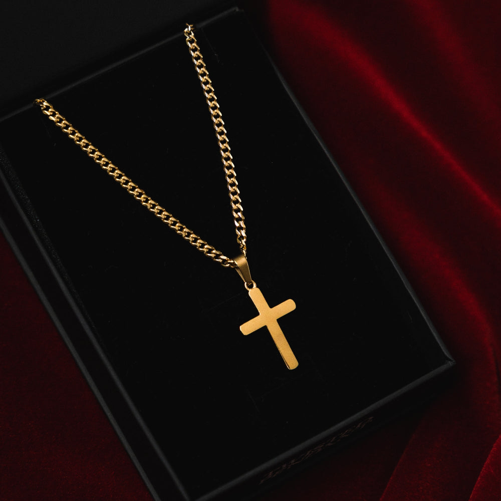 Gold chain necklace with a cross pendant on a black box with red fabric background