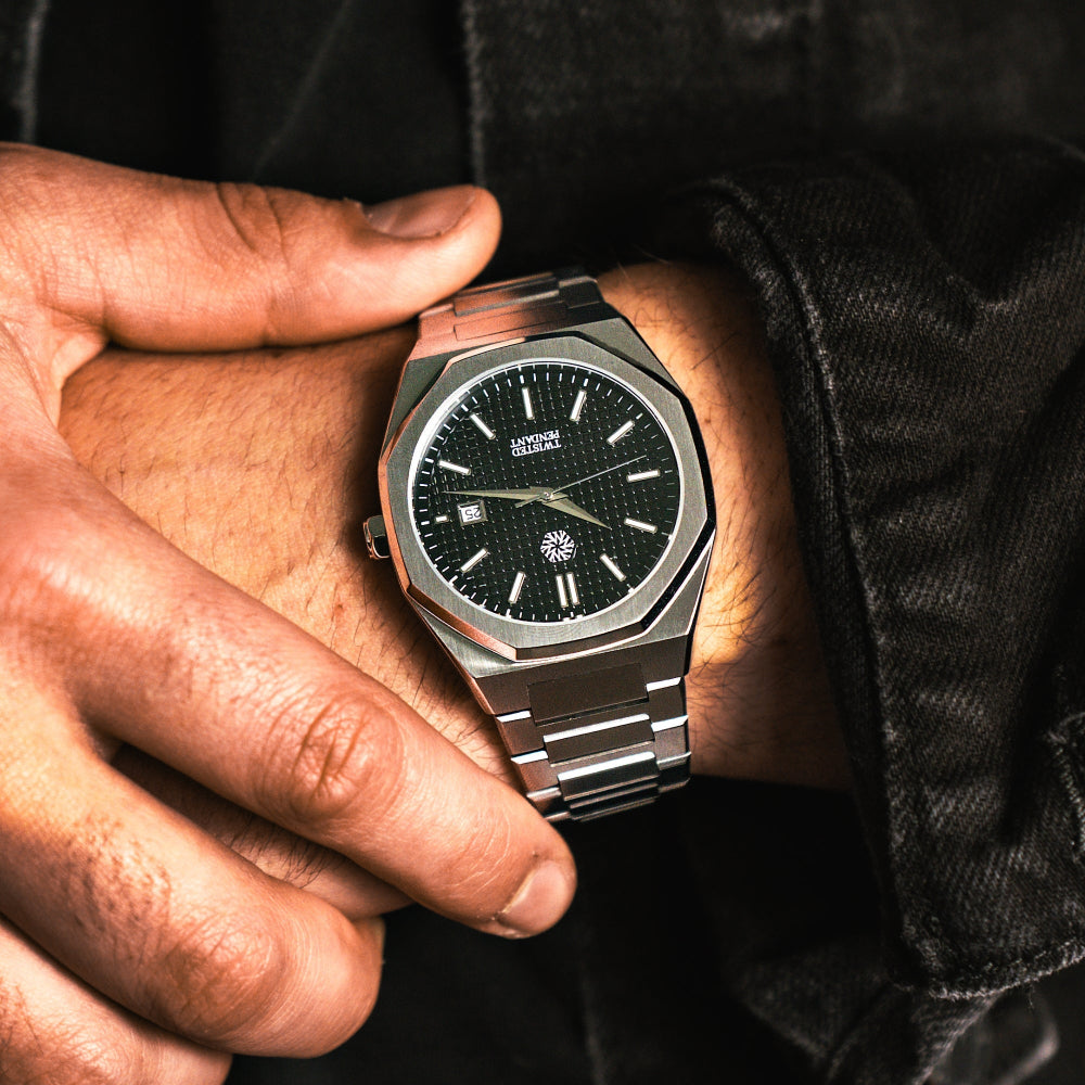 Close-up of a person wearing a luxury watch with a black face and silver case.