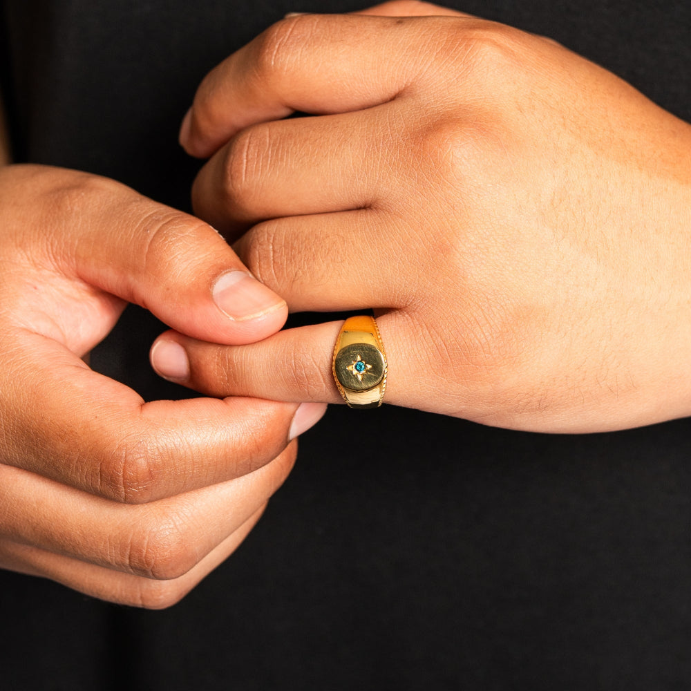 Close-up of a hand wearing a gold ring with a blue gemstone on a black background