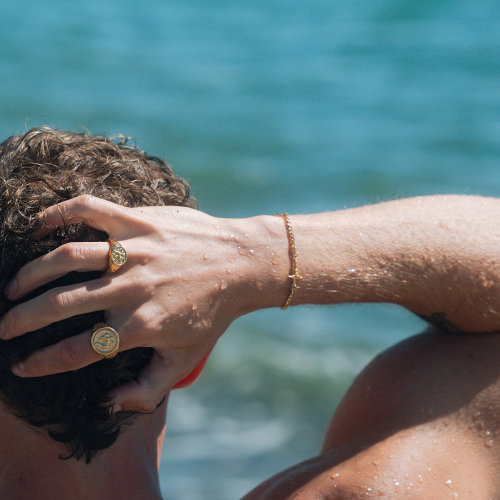 Person with gold ring and bracelet against a blurred blue water background