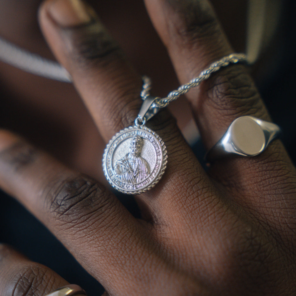 Close-up of a hand wearing a silver necklace with a pendant featuring a portrait.