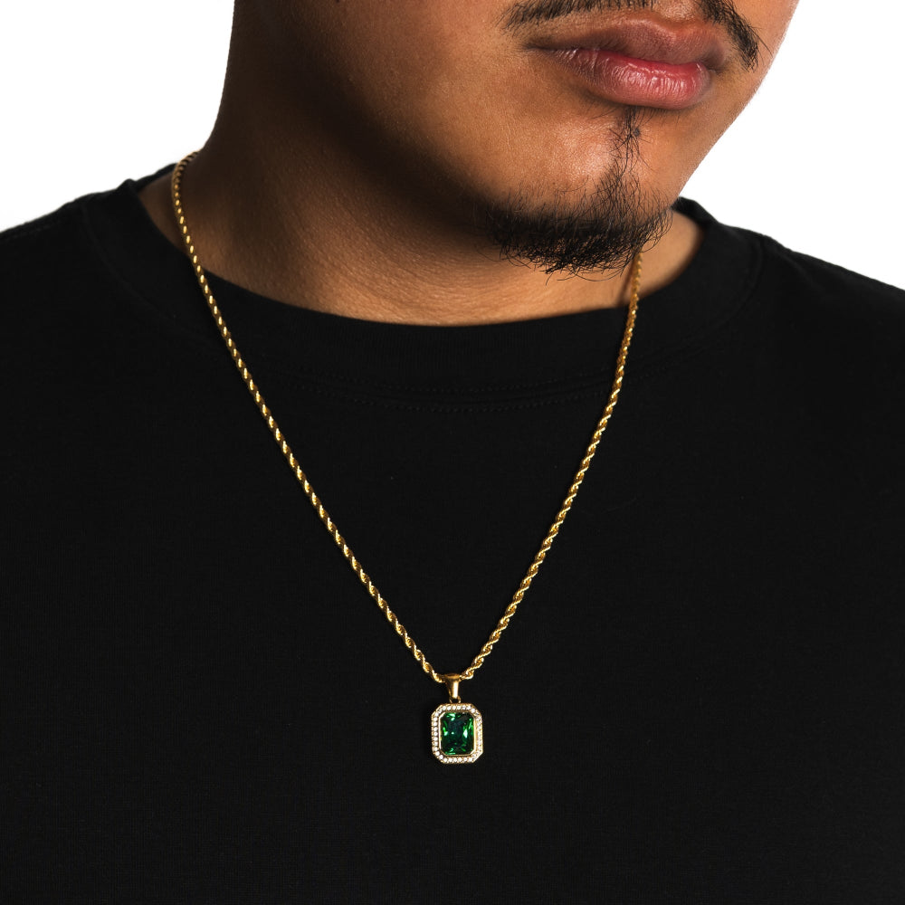 Man wearing a gold chain with a green gemstone pendant on a black background