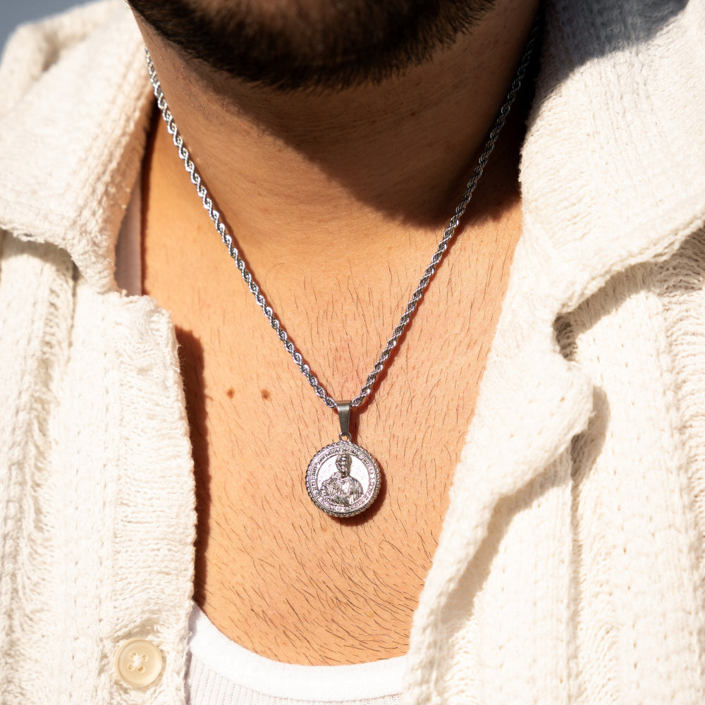Close-up of a silver necklace with a pendant worn by a person in a light-colored jacket.