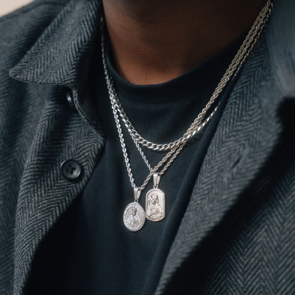 Person wearing multiple silver necklaces with pendants on a dark background