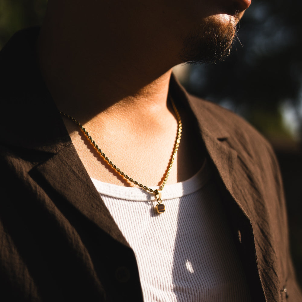 Person wearing a gold necklace with a pendant, blurred background