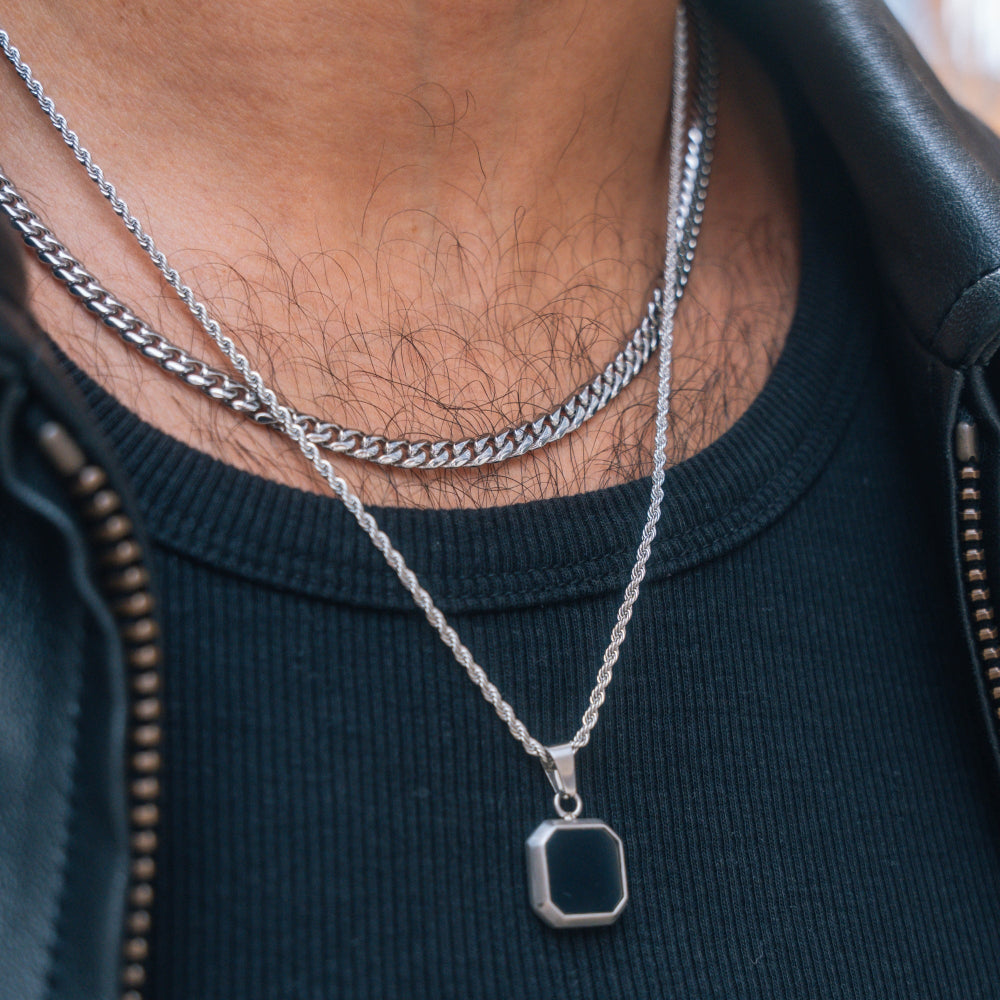 Close-up of a person wearing two silver necklaces with a black shirt.